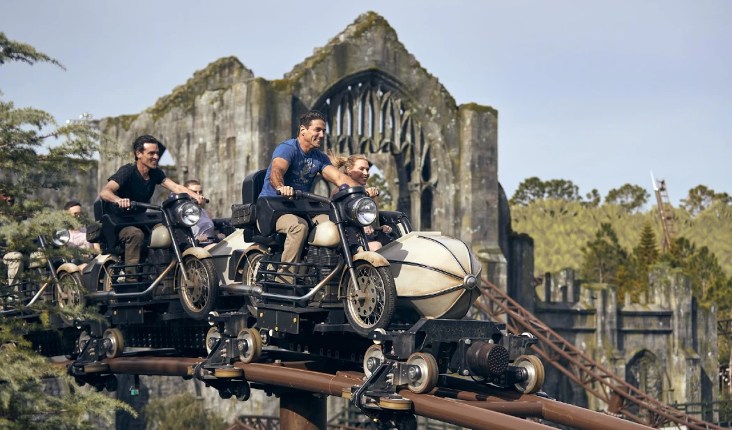 Riders enjoy a thrilling roller coaster designed to look like motorbikes, set against a fantastical castle backdrop