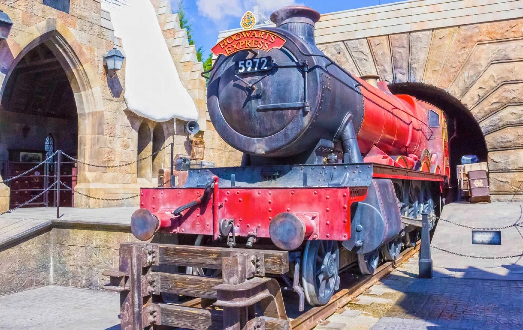 A bright red steam engine labeled 'Hogwarts Express' stands outside a stone archway