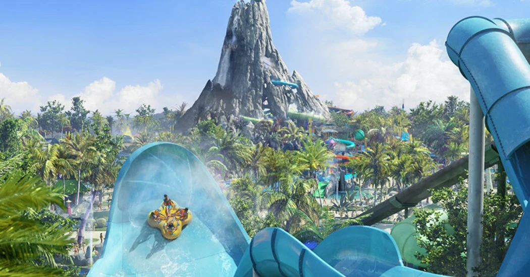 A water slide descends into a tropical water park featuring lush palm trees and a majestic volcano backdrop