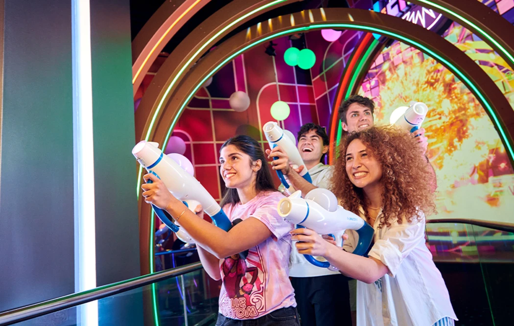 Four people hold futuristic water guns, posed playfully against a neon-lit background