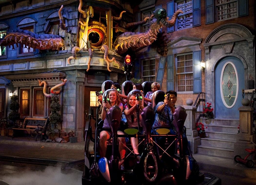 A group of people on a dark amusement ride, surrounded by animated creatures and bright lights