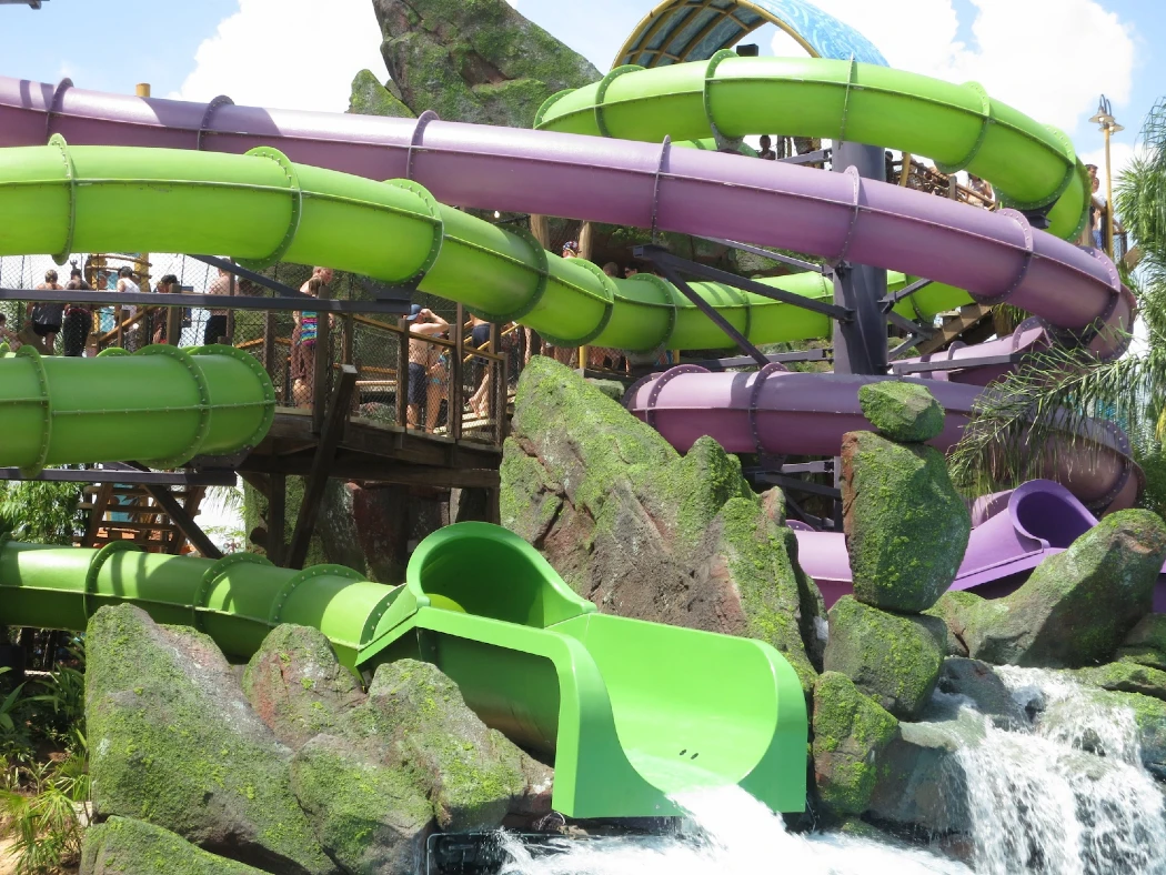 Colorful water slides twist and turn above a rocky landscape, with visitors eagerly awaiting their turn to ride
