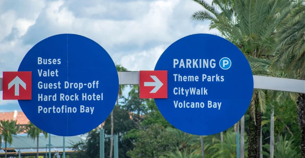 Blue directional signs indicating parking and guest services for a hotel, highlighting bus routes and nearby attractions like Volcano Bay