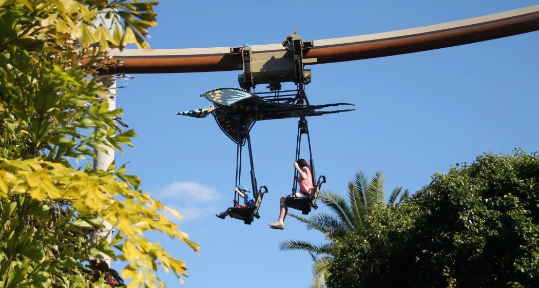 Two children ride on a colorful bird-shaped gondola suspended on a ski lift