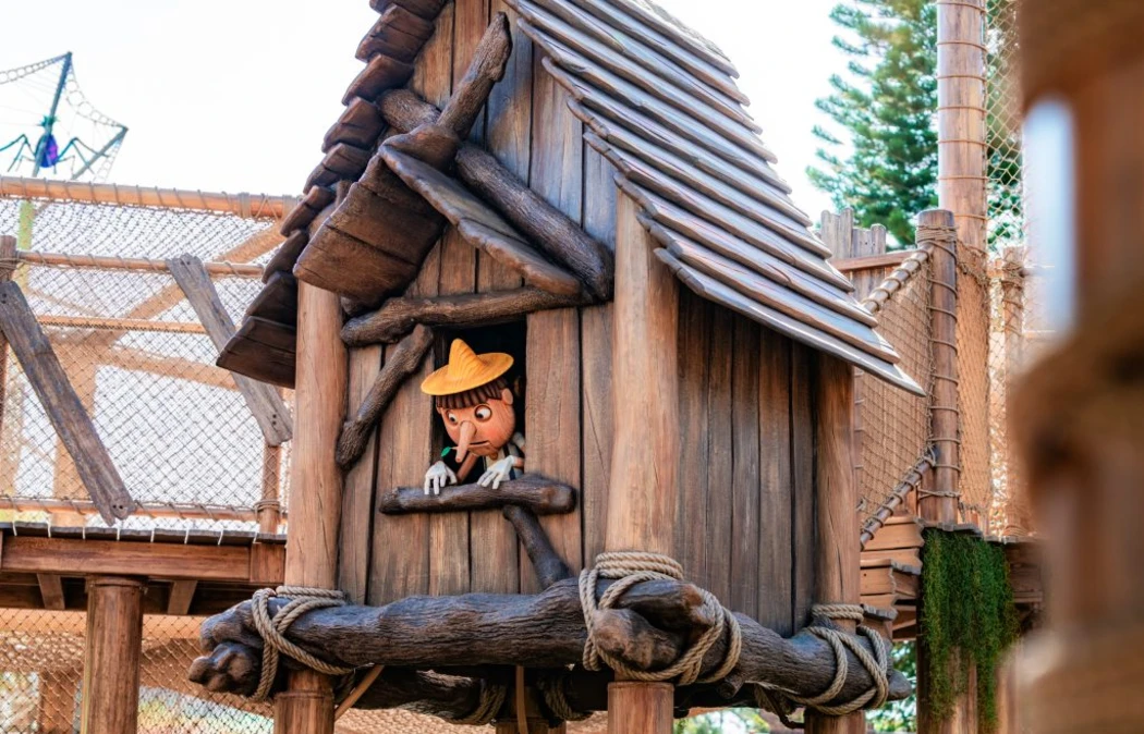 A long-nosed cartoon character with a yellow hat peeking out the window from a wooden tree house