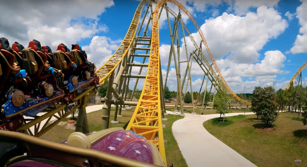 A roller coaster climbs a steep yellow track under a blue sky