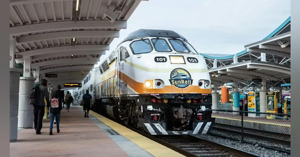 A passenger waiting to board a sleek, yellow, and black Sunrail train at a station