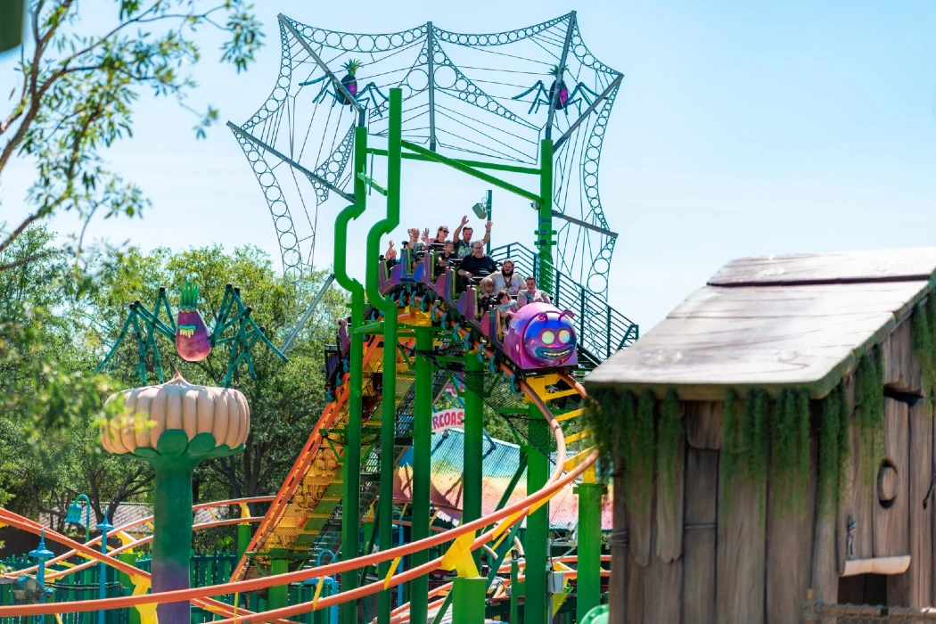 A colorful caterpillar-faced roller coaster with excited riders waving as they ascend