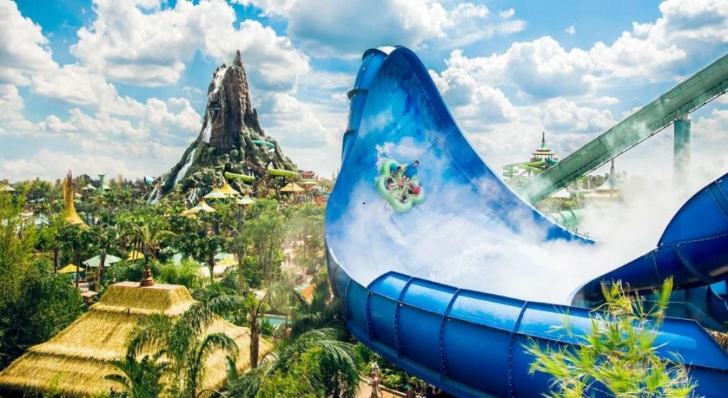 The Volcano Bay water park having blue slide, lush tropical landscaping, and a volcano mountain