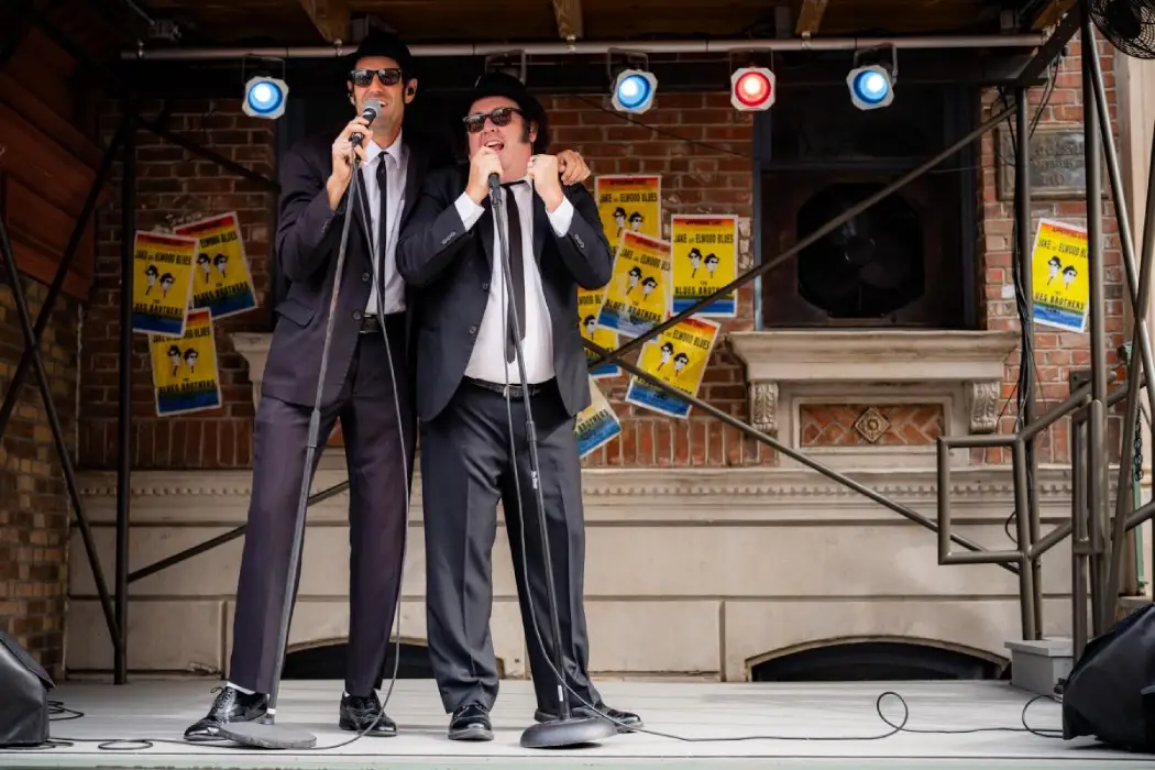 2 men dress in black suits singing and dancing