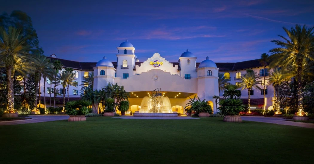 The Hard Rock Hotel entrance at dusk, featuring a fountain, palm trees, and distinctive domes illuminated by soft lighting