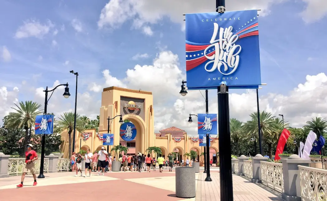 Colorful banners celebrating the 4th of July adorn the entrance to Universal Studios, with guests enjoying a sunny day in Orlando
