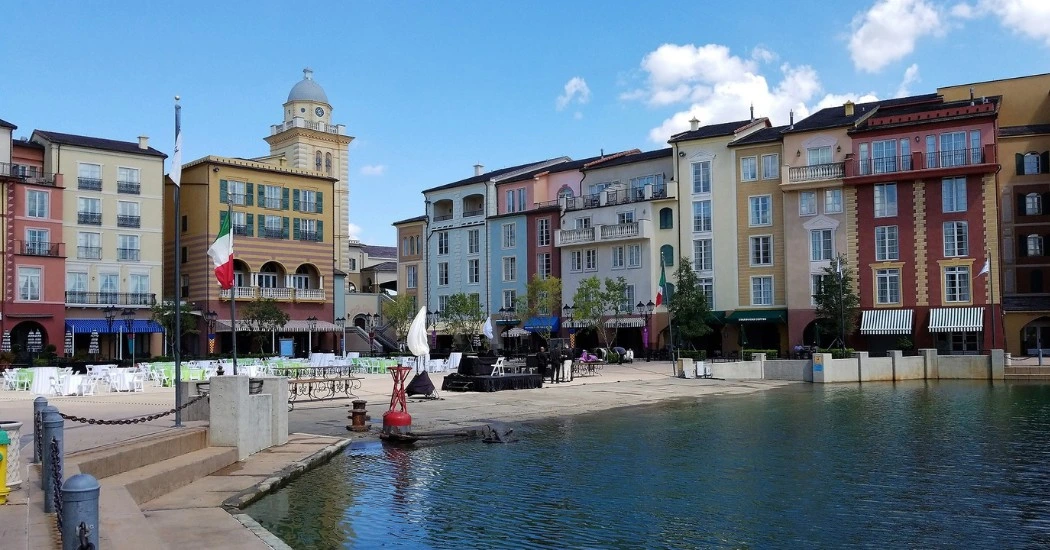Vibrant waterfront scene featuring colorful Mediterranean-style buildings, outdoor dining, and a calm lake under a clear blue sky