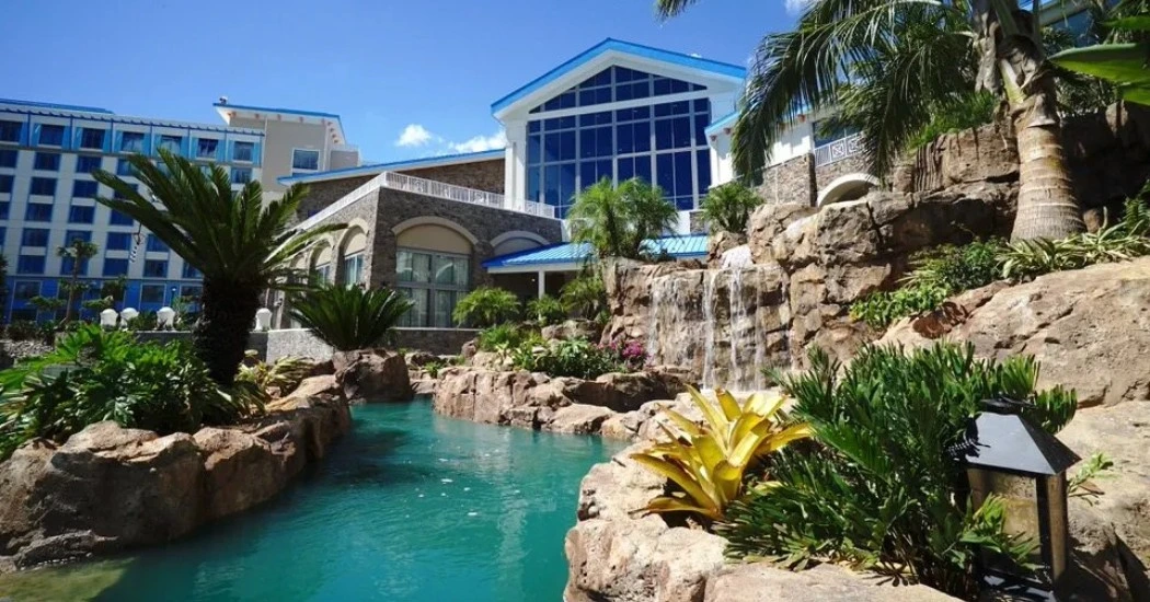 A scenic resort featuring a turquoise pool, lush greenery, tropical plants, and a waterfall
