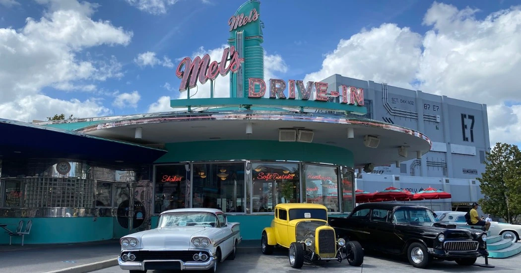 Mel's Drive-In features classic cars parked outside a retro diner with a turquoise facade