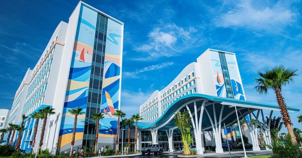 Brightly colored hotel facade featuring beach-themed murals, palm trees, and a sunny sky, inviting guests to a tropical getaway