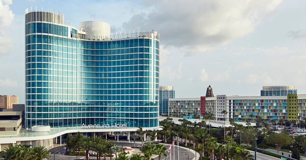 View of Aventura Hotel, a modern glass building surrounded by palm trees and colorful adjoining structures