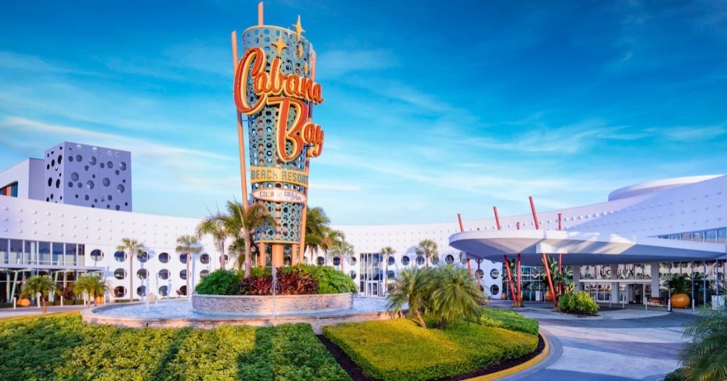 Cabanas Bay Beach Resort entrance featuring a vibrant sign, modern architecture, and tropical landscaping under a clear blue sky