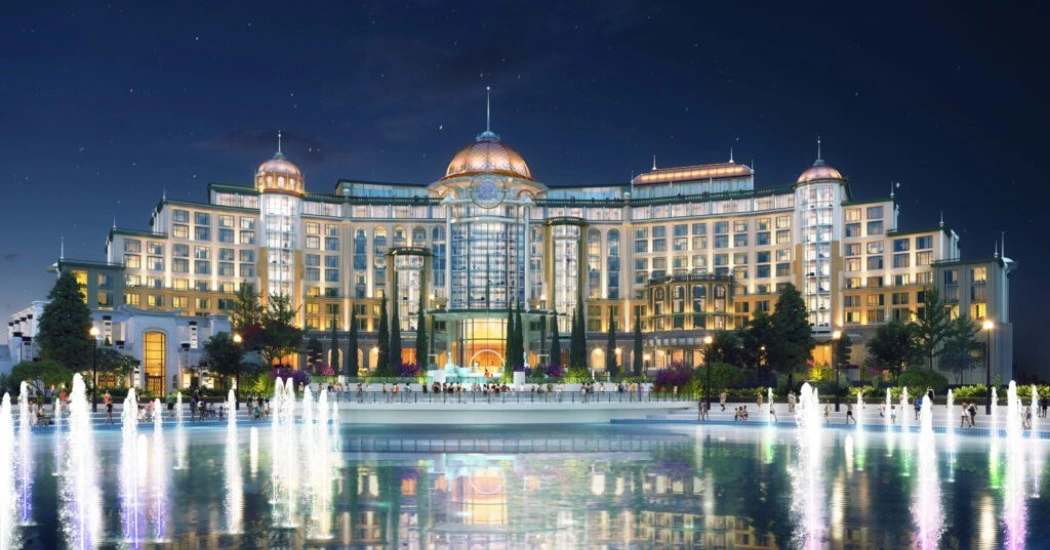 Grand hotel exterior at night, featuring illuminated architecture and a fountain display, reflecting in a tranquil pond