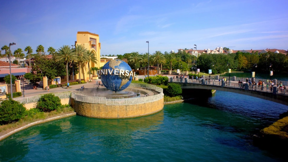 Universal Studios entrance featuring a large globe and palm trees, with visitors walking along a bridge and enjoying the scenic park