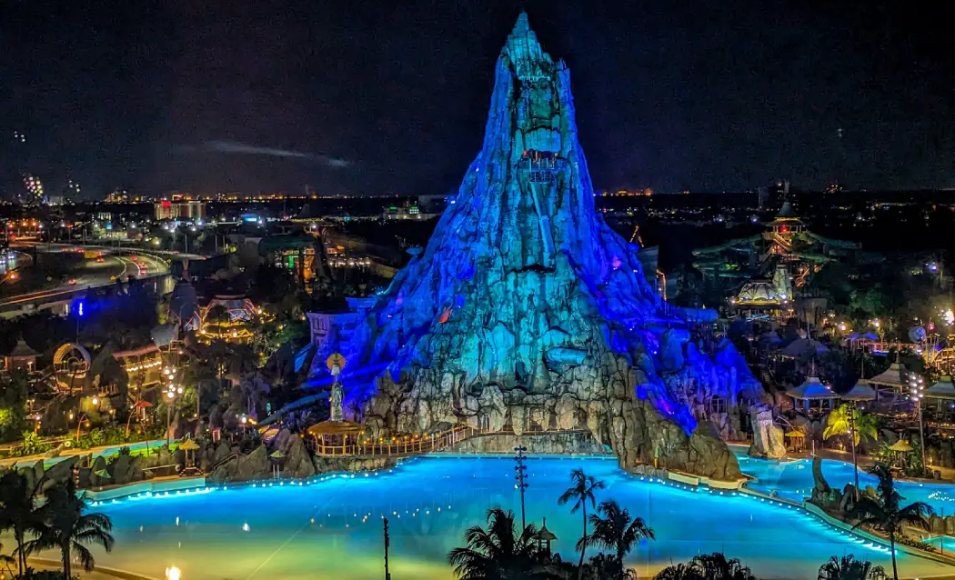 Nighttime view of Volcano Bay water park featuring a large illuminated volcano surrounded by palm trees and a glowing lagoon