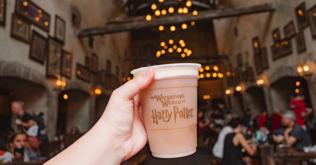 A man holding the Wizard World of Happy Potter glass, Leaky Cauldron in the background